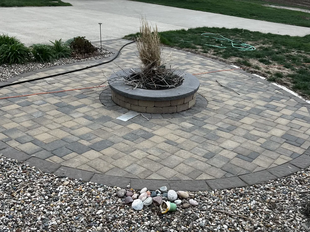 Circular paver patio with a block fire pit ring and stone cap by Larkin Landscape and Design