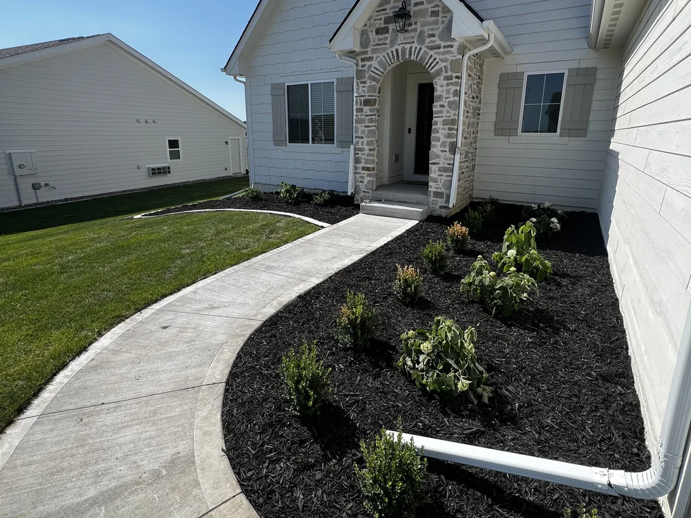 Front-entry planting beds in fresh dark mulch and new sod along a curved walkway, installed by Larkin Landscape and Design