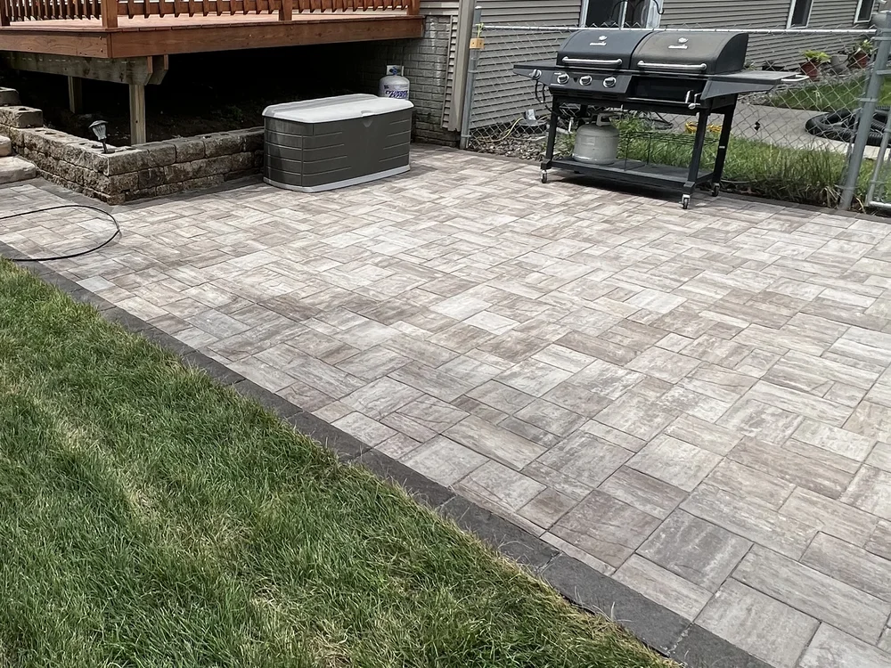 Paver patio with a charcoal border course set beneath a raised deck, built by Larkin Landscape and Design