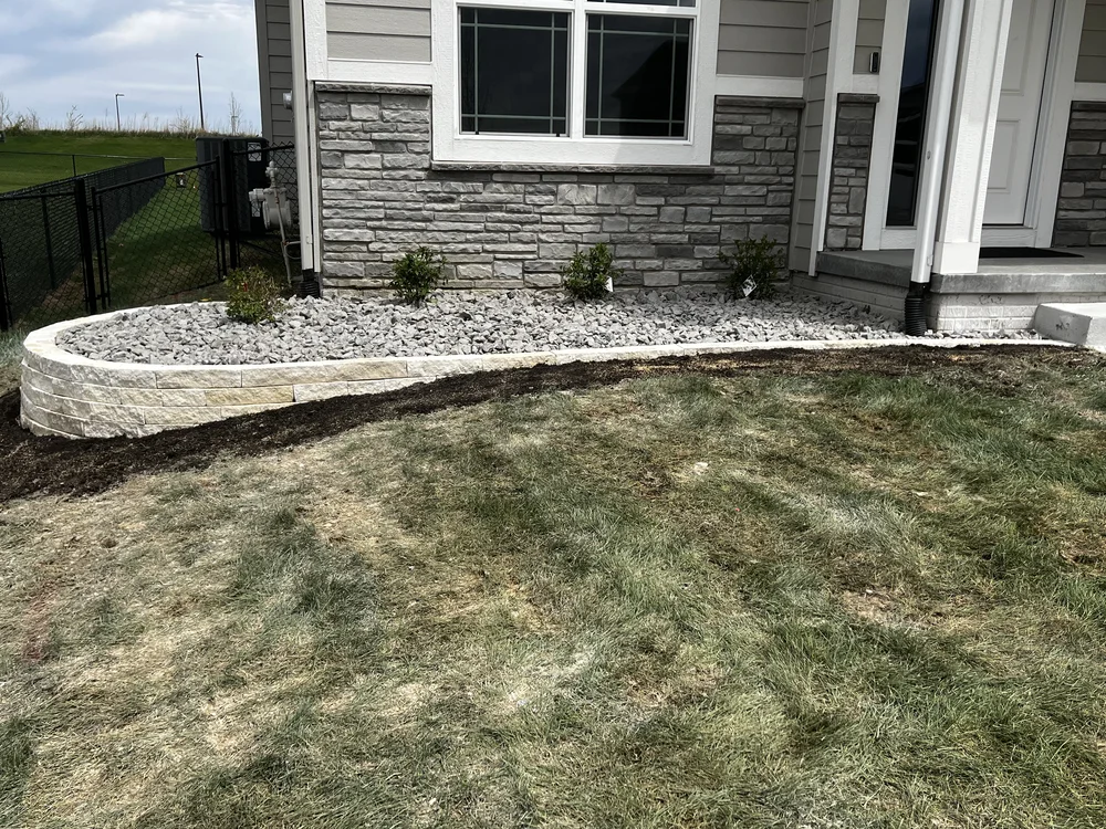 Curved stacked-stone landscape wall with a rock mulch bed and new plantings by Larkin Landscape and Design