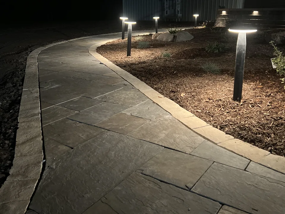 Low-voltage landscape lighting on beds and a path at night by Larkin Landscape and Design