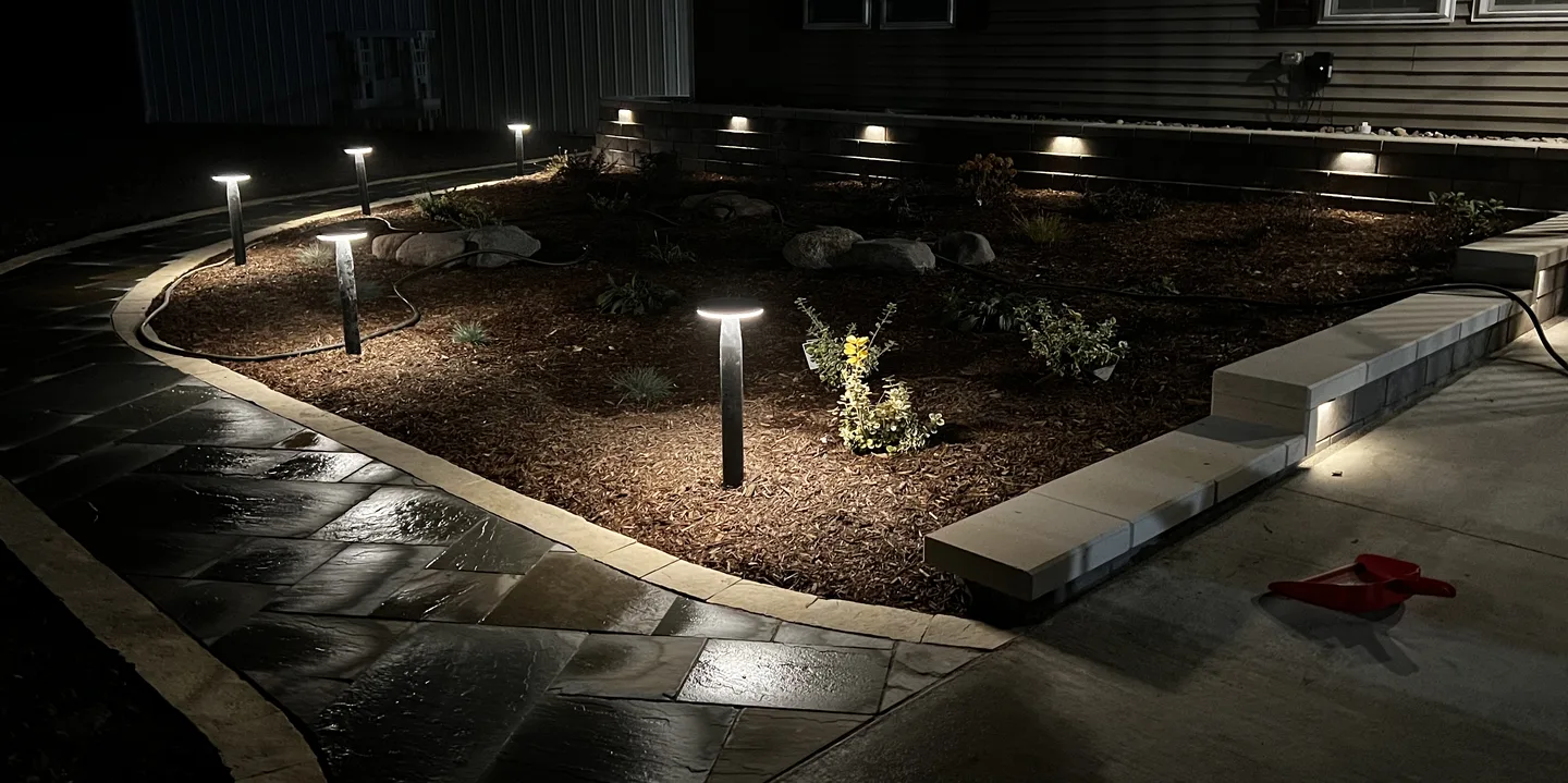 Low-voltage path lights and under-cap wall lights glowing along a planting bed at dusk, installed by Larkin Landscape and Design