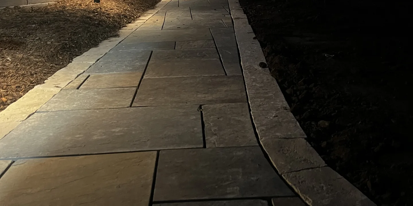 Stone walkway lit by low-voltage path lights at night by Larkin Landscape and Design