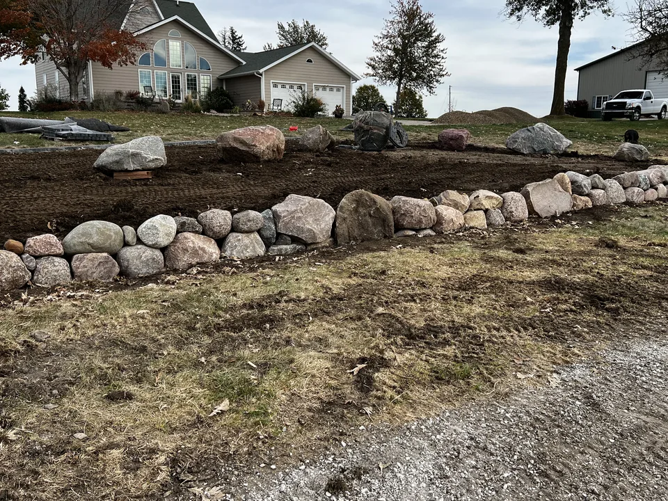 Boulder retaining wall under construction with a graded planting bed behind it by Larkin Landscape and Design
