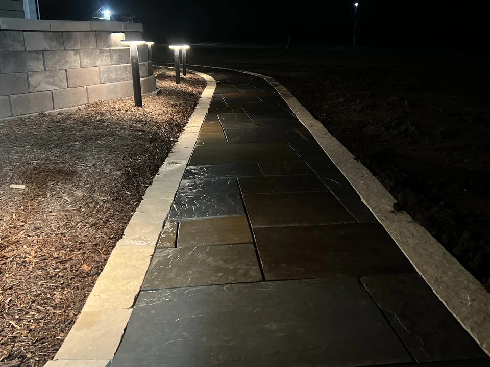 Paver walkway lit for evening use through a planted yard by Larkin Landscape and Design
